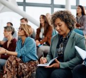 Mature entrepreneur writing in her notebook while attending a business seminar at conference hall.
